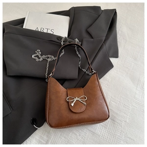 Detail of a brown crescent handbag featuring a silver bow clasp and elegant chain strap