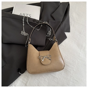 Detail of tan leather shoulder bag with silver bow buckle and elegant metal chain strap