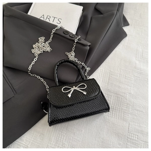 Detail of black faux crocodile leather mini bag with silver metal bow and chain strap