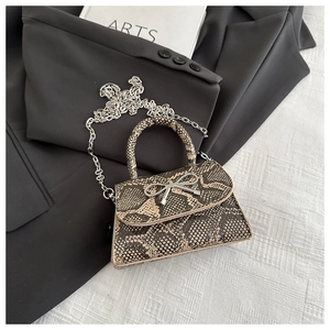Detail of crocodile texture small square bag with silver metal bow and chain strap