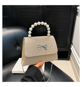 Detail of champagne gold glitter evening bag with pearl handle and metal bow buckle