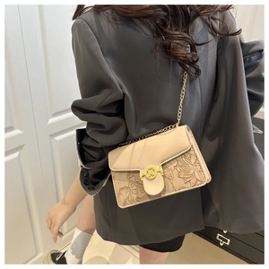 Détail d'un sac bandoulière beige avec relief floral et chaîne dorée sur mannequin