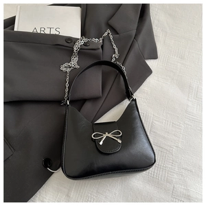 Detail of black leather hobo bag with silver bow buckle and metal chain strap on fabric