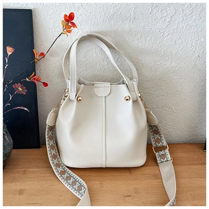 Close-up of beige bucket bag showing pebble leather texture and colorful woven strap