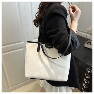 Detail of minimalist tote bag showing white crinkled fabric and black leather handles