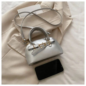 Detail of silver metallic shell bag with belt accents on a beige blazer and book
