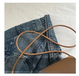 Dettaglio di una tracolla in pelle marrone su denim e tessuto bianco con texture