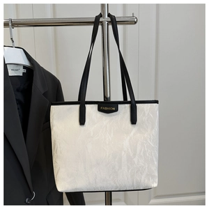 Detail of white wrinkled texture tote bag with gold Fashion emblem and black strap