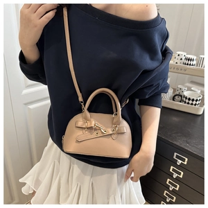 Close-up of beige shell bag with decorative leather strap and golden metal buckle details