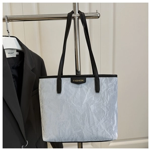 Detail of grey tote bag with paper-like texture, black handles and Fashion label