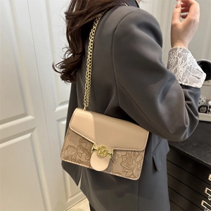 Sac bandoulière rétro beige avec gaufrage floral et boucle M dorée porté par un modèle