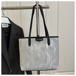 Detail of silver tote bag with metallic crinkle texture and black leather handles