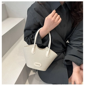 Détail du sac seau tressé beige avec plaque Fashion tenu par un mannequin sur escalier