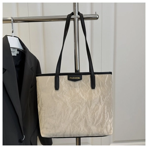 Detail of cream pleated tote bag with black handles and fashion tag on display stand