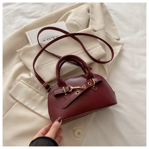 Close-up of wine red shell handbag with gold buckle and matte leather texture detail