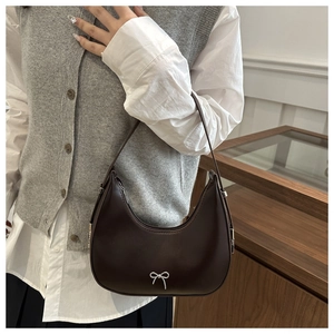 Detail of dark brown crescent bag with silver bow accent on model with casual outfit
