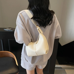 Minimalist beige crescent hobo shoulder bag with adjustable strap worn by a model