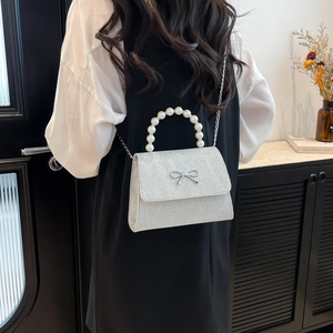 Silver sequin crossbody bag with pearl handle and metal bow, shown on model back