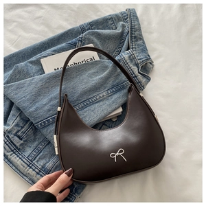 Close-up of a brown half-moon hobo bag with a silver bow detail on denim jacket