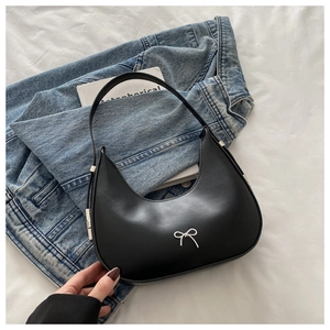 Detail of black leather underarm bag with silver bow accent on denim jacket