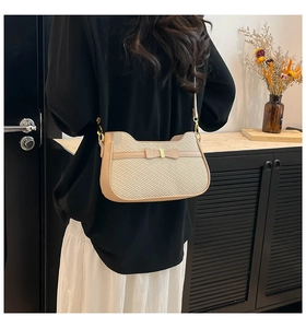 Detail view of beige crossbody bag featuring woven texture and decorative bow on model