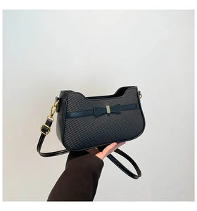 Detail of black crossbody bag featuring a woven texture and bow with gold metal buckle