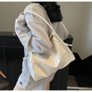 Détail latéral d'un sac cabas en cuir verni blanc avec nœud décoratif sur la bandoulière