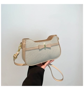 Detail of the elegant woven pattern, leather bow, and gold buckle on the cream handbag