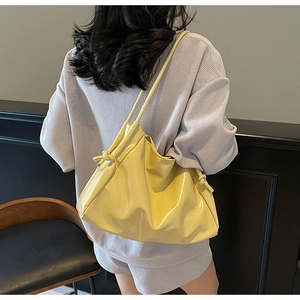 Detail of light yellow glossy leather tote bag with knot strap and pleated cloud design