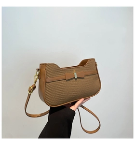 Detail of warm brown woven handbag featuring a leather trim and delicate bow accent