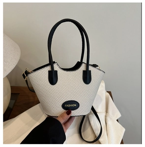 Gros plan du sac seau tissé avec bordure en similicuir noir et logo doré brillant