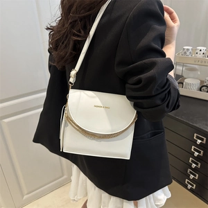 Sac bandoulière minimaliste en cuir blanc avec chaîne dorée porté par un modèle