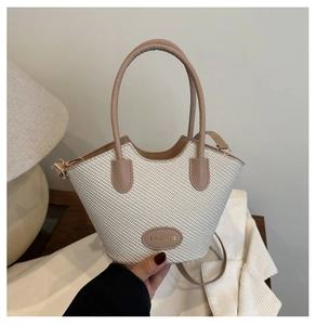 Détail d'un sac seau tissé beige avec anses en cuir et logo doré FASHION