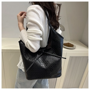 Detail of black woven leather tote bag featuring a decorative bow tie closure