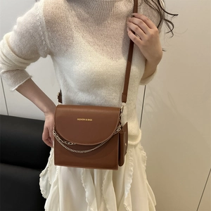 Sac bandoulière minimaliste en cuir marron avec chaîne dorée présenté sur modèle