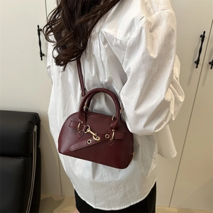Chic burgundy shell-shaped leather handbag with belt decor shown on a model