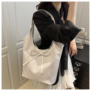 Close-up of white woven tote bag with bow detail worn by model in professional attire