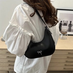 Minimalist black crescent shoulder bag with silver bow detail worn by a model