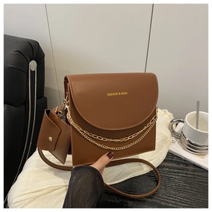 Brown leather crossbody bag with dual chain decor and small pouch on white fabric