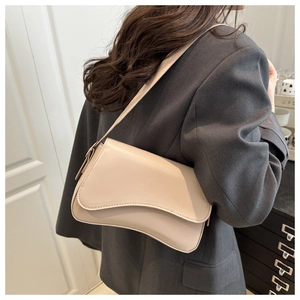 Minimalist beige crossbody bag with a unique curved flap design shown on a shoulder