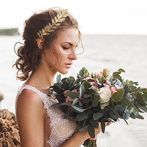 Close-up of golden metal leaf branch hairband on bride wearing white lace dress