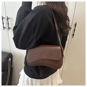 Close-up of a brown wave-flap shoulder bag worn over a black outfit for styling