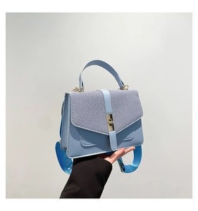 Détail du sac à main bleu clair avec texture tissée grise et fermoir rotatif doré