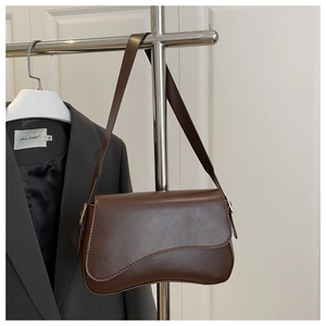 Detail of a dark brown leather saddle bag featuring an asymmetric flap and gold hardware
