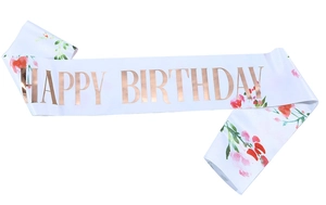 Detailaufnahme einer weißen Satinschärpe mit roségoldener Happy Birthday Prägung und Blumen