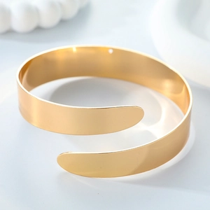 Minimalist gold spiral open arm cuff with high-polished metallic finish on a white background