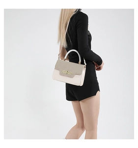 Detail of light pink and beige crossbody bag featuring a woven flap and gold buckle