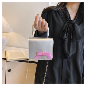 Detail of silver metallic mini square bag with a pink bow and a fine chain strap