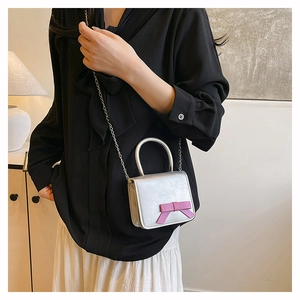 Silver mini crossbody bag with pink bow detail and metal chain strap shown on model