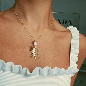 Élégant collier à pendentif feuille dorée et perles blanches sur le cou d'une femme